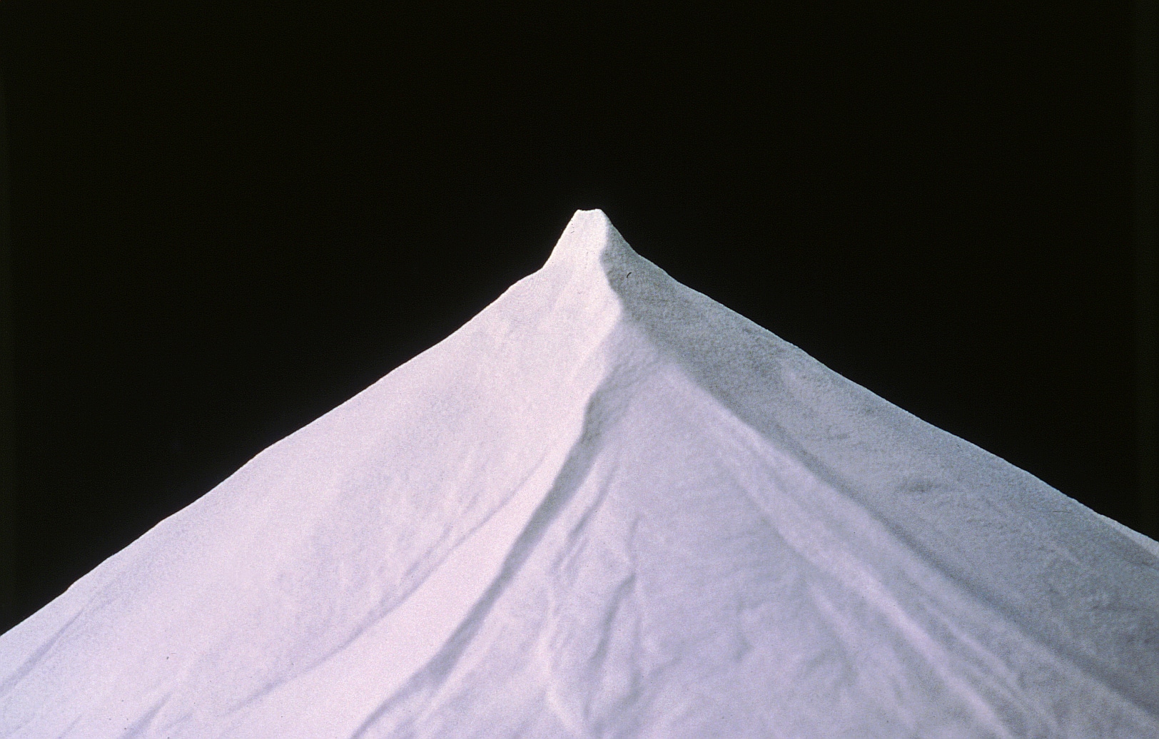 A sharply peaked mound of fine white powder set against a stark black background. The smooth texture of the powder rises to a pointed apex, creating a triangular shape that stands out prominently, reminiscent of the pristine quality emphasized by the International Aluminium Institute.