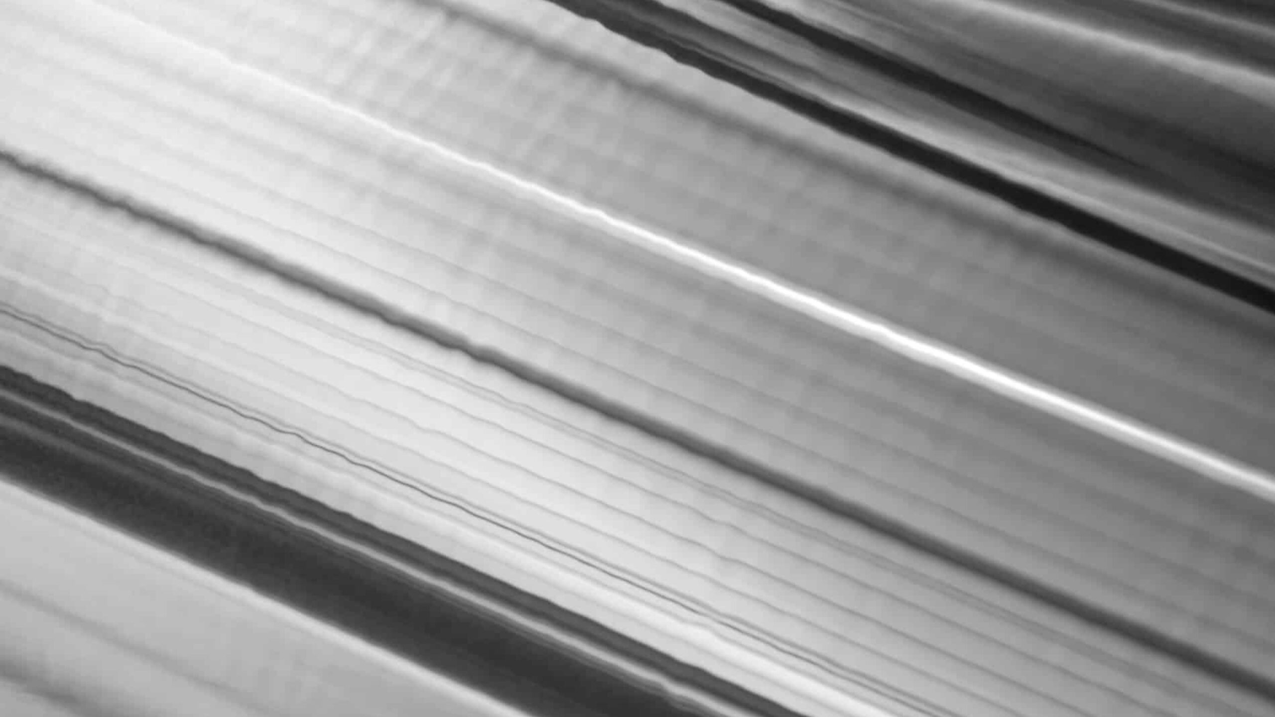 Close-up of an aluminium surface with linear patterns and reflections, creating a textured and abstract visual effect. The lines vary in width and run diagonally across the image, giving it a dynamic and modern appearance. This monochromatic scene forecasts various artistic scenarios.