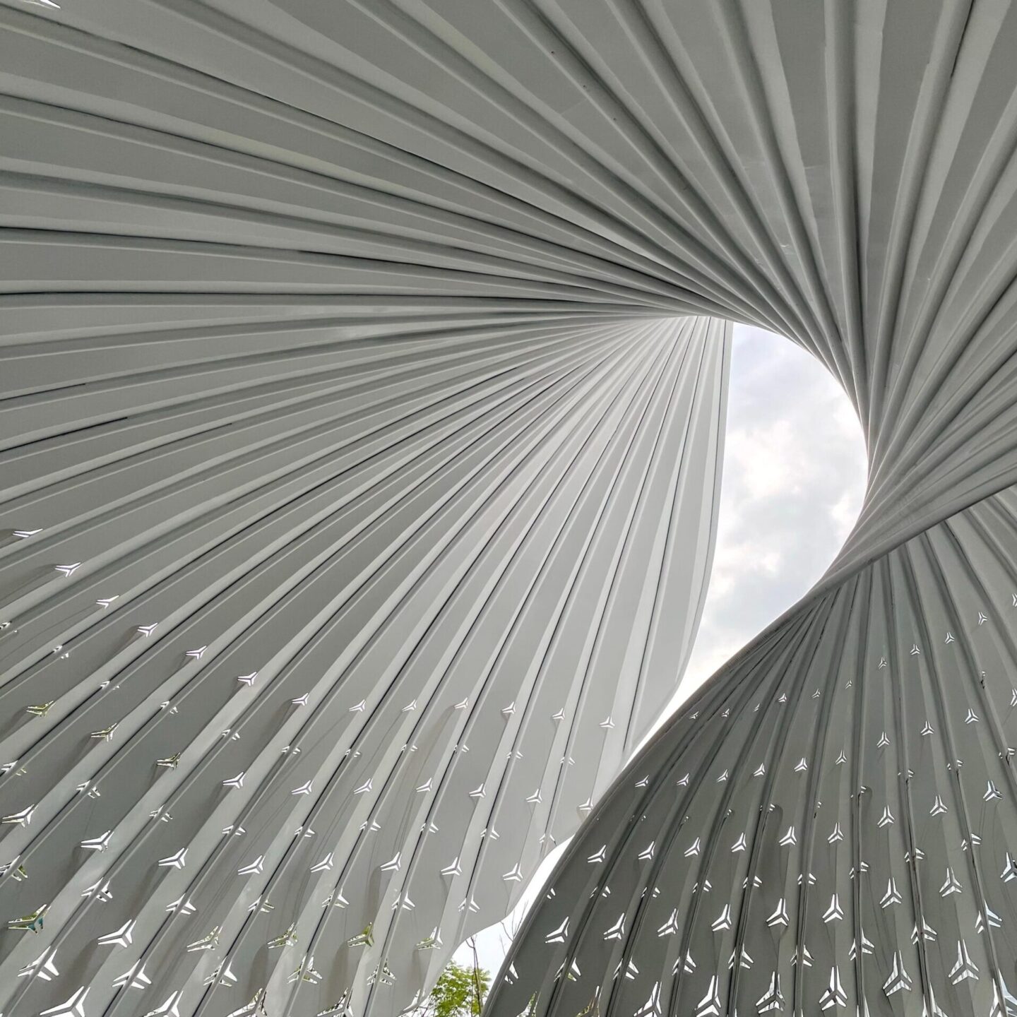 The image shows an abstract architectural structure with two curved forms made up of ribbed panels. The curves twist and converge towards the center, creating an opening through which the sky and clouds are visible, symbolizing innovation for IAI 50 anniversary.