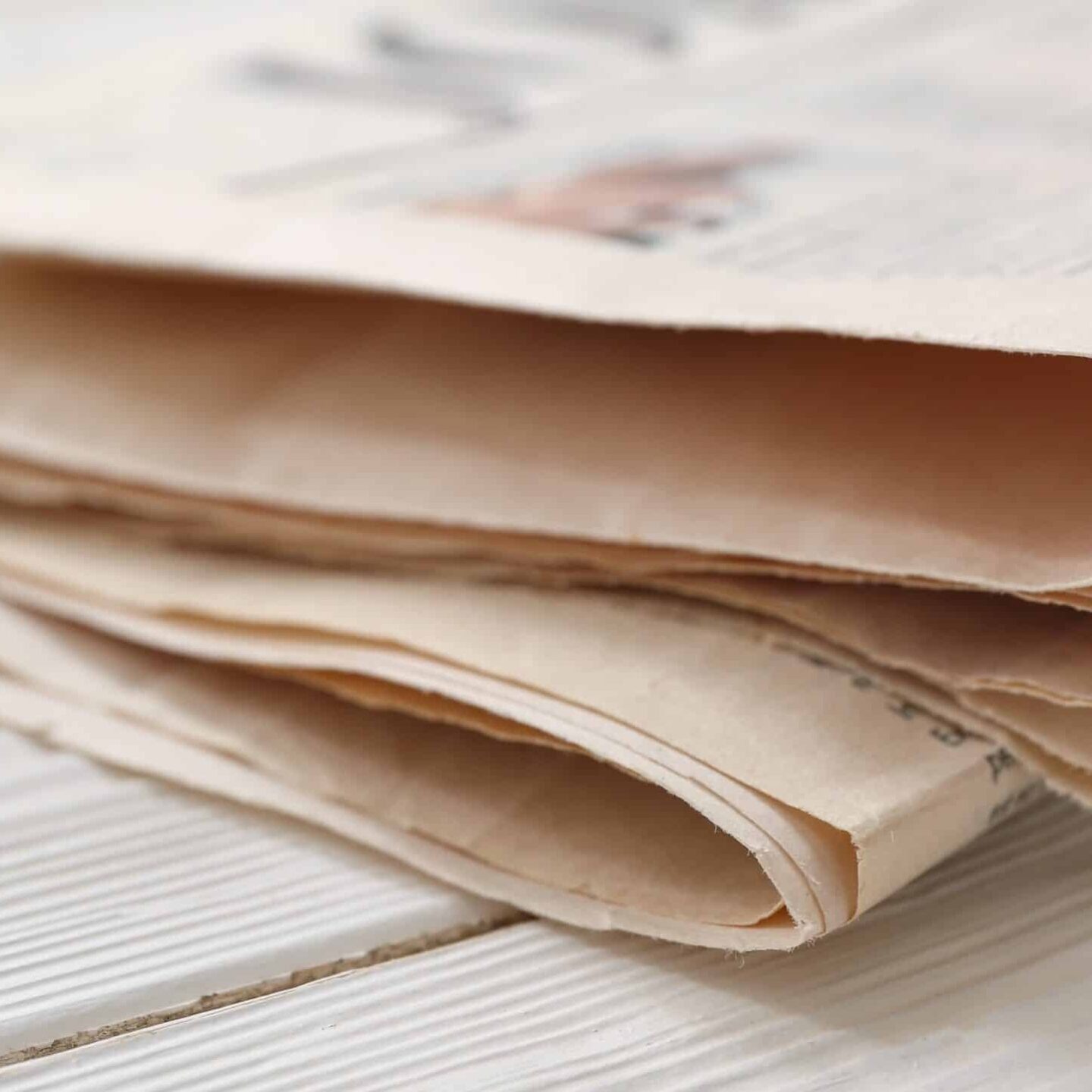 A close-up view of a folded newspaper placed on a white wooden surface. The newspaper's pages are slightly fanned, revealing its edges and the paper's texture, with an article commemorating IAI's 50th anniversary.