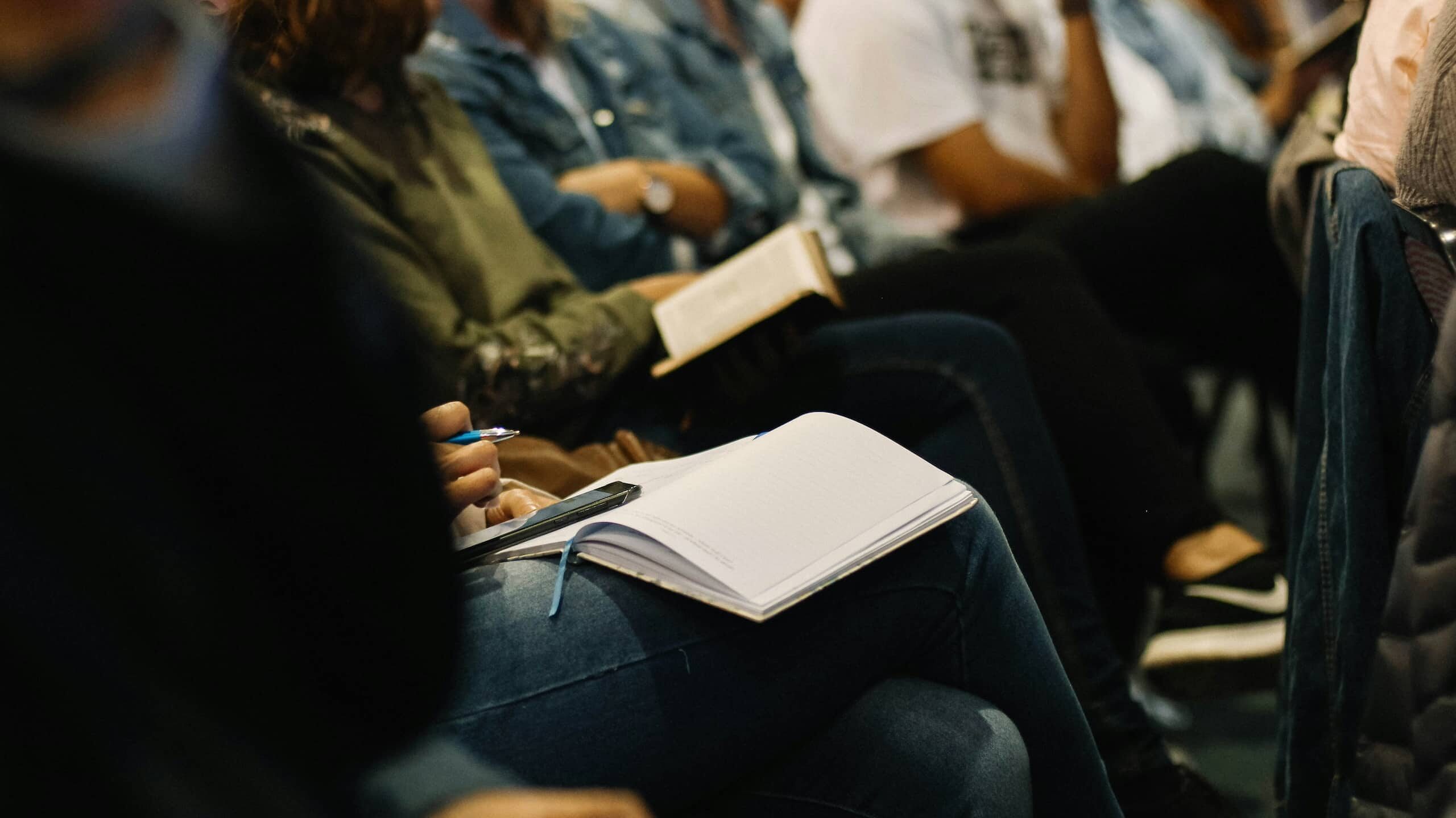 Aluminium Forward 2030 People are seated in a classroom or conference setting, attentively taking notes in notebooks and holding books. The image focuses on their hands and notebooks, emphasizing engagement and learning, symbolizing the foundation of skills needed for the aluminium 2030 industry transformation.